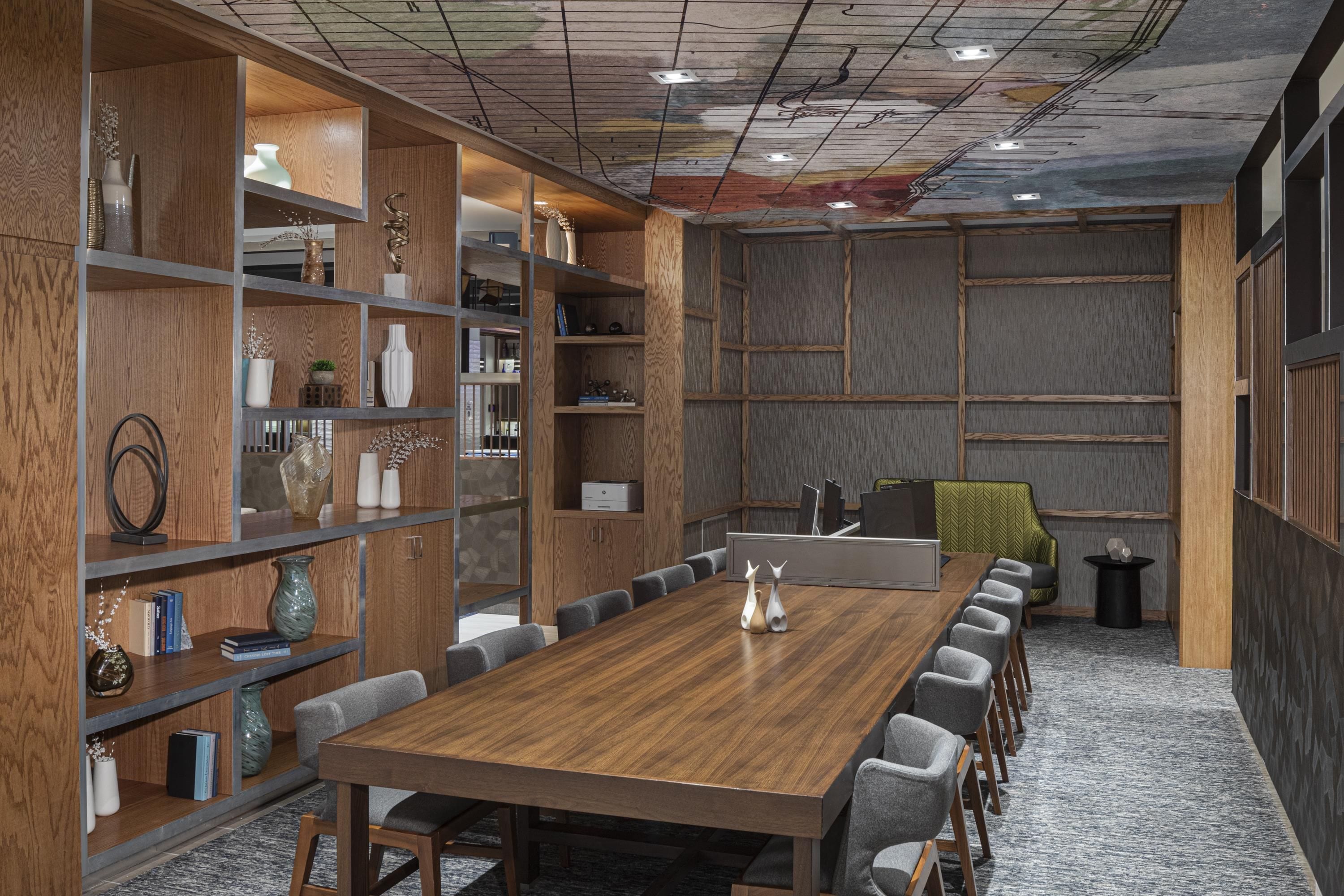 A conference room with a long wooden table, grey chairs, and built-in wooden shelving with various decorative items.