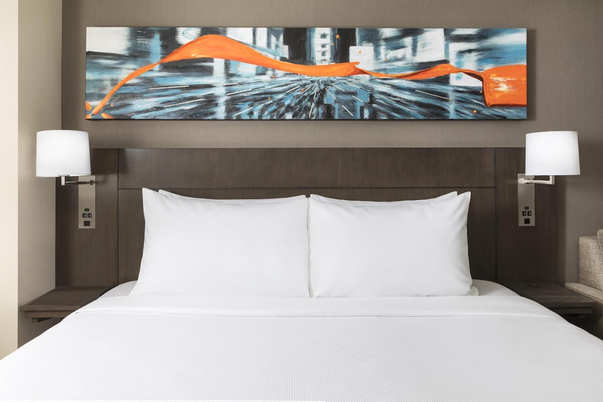 Ein Hotelzimmer mit einem großen Bett, zwei Nachttischlampen, einem Wandbild und einem Holzkopfteil.