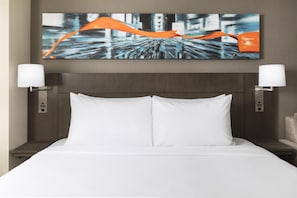 Habitación de hotel con una cama grande, dos lámparas de noche, un cuadro en la pared y un cabecero de madera.