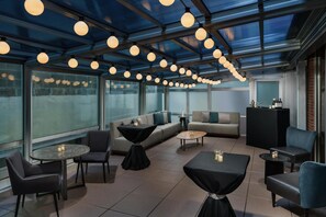 Ein moderner Lounge-Bereich mit runden Tischen, Sofas und Sesseln, großen Fenstern und einer Decke mit Pendelleuchten.