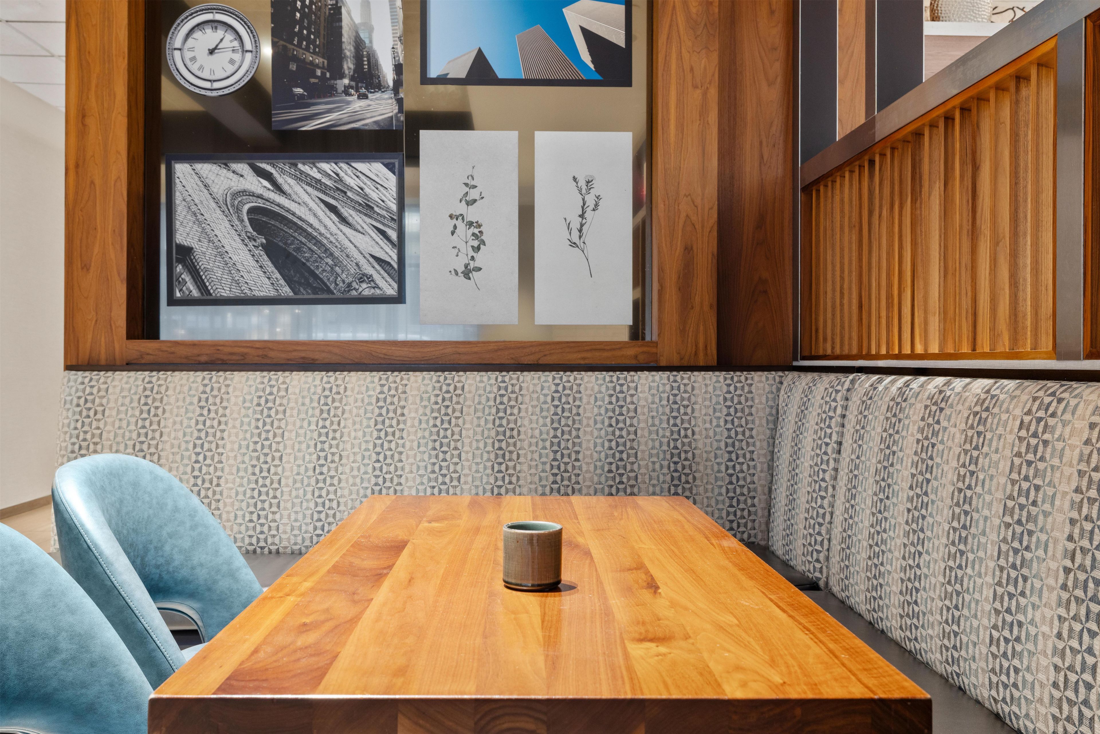 A wooden table with a cup, blue chairs, and a patterned wall with framed pictures.