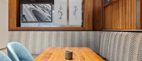 A wooden table with a cup, blue chairs, and a patterned wall with framed pictures.