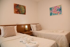 A hotel room with two beds, each with a pillow and a blanket. There is a painting on the wall and a nightstand with a lamp. - Villa Caracol (Ipojuca)