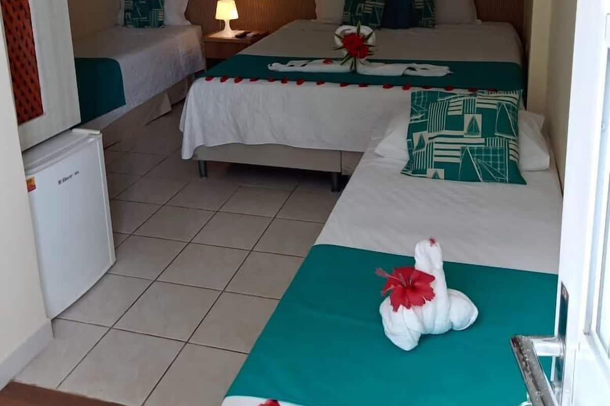 A hotel room with two beds, a nightstand with a lamp, a refrigerator, and a painting on the wall.