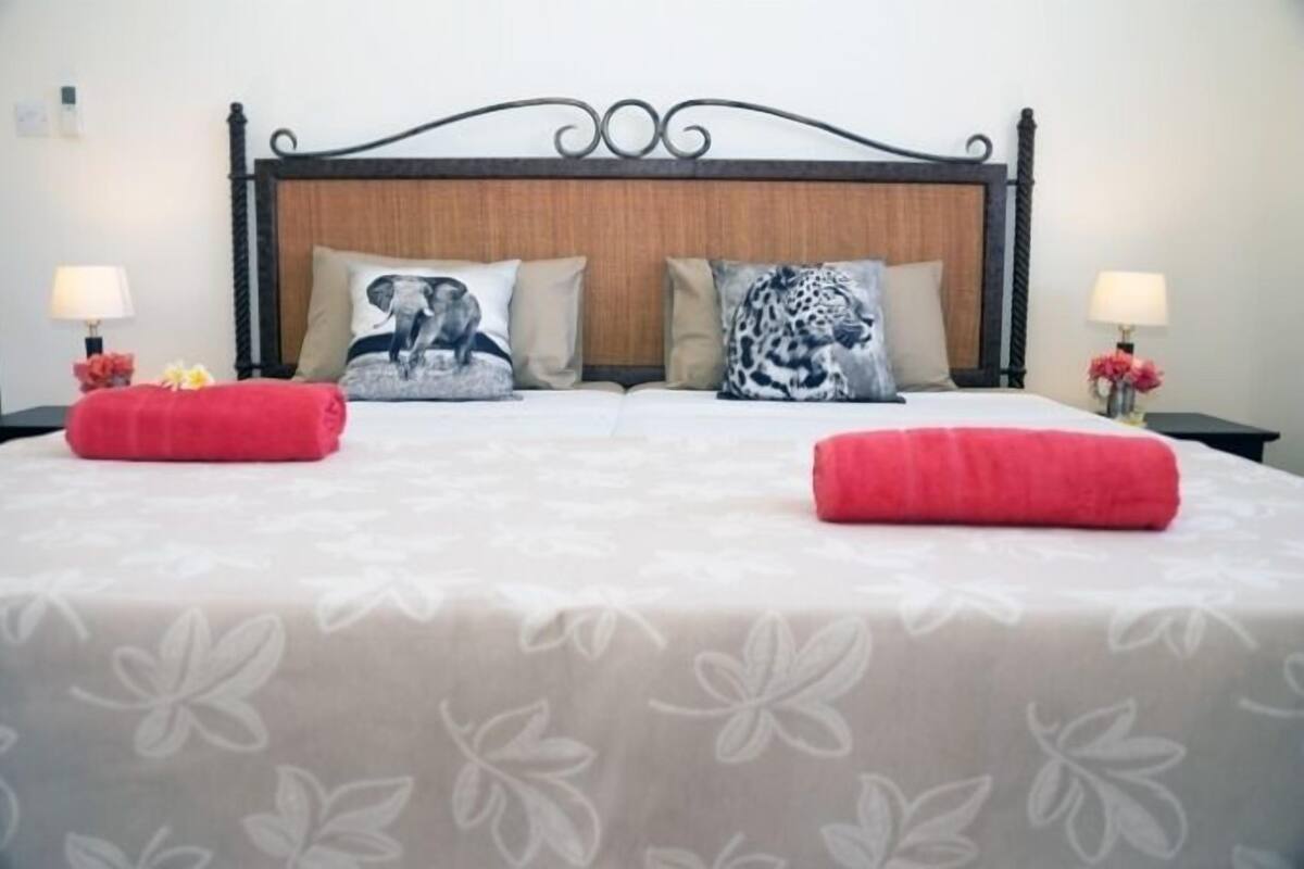 A neatly made bed with a floral bedspread, two pillows with animal prints, and two red towels.