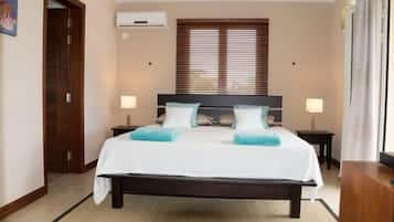 Quarto de hotel com uma cama grande, duas mesas de cabeceira, uma janela com persianas e uma porta.