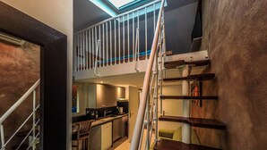 Eine Treppe führt zu einem Balkon im zweiten Stock mit Geländer. Eine Küchenzeile ist im zweiten Stock sichtbar, einschließlich Spüle und Schränke.