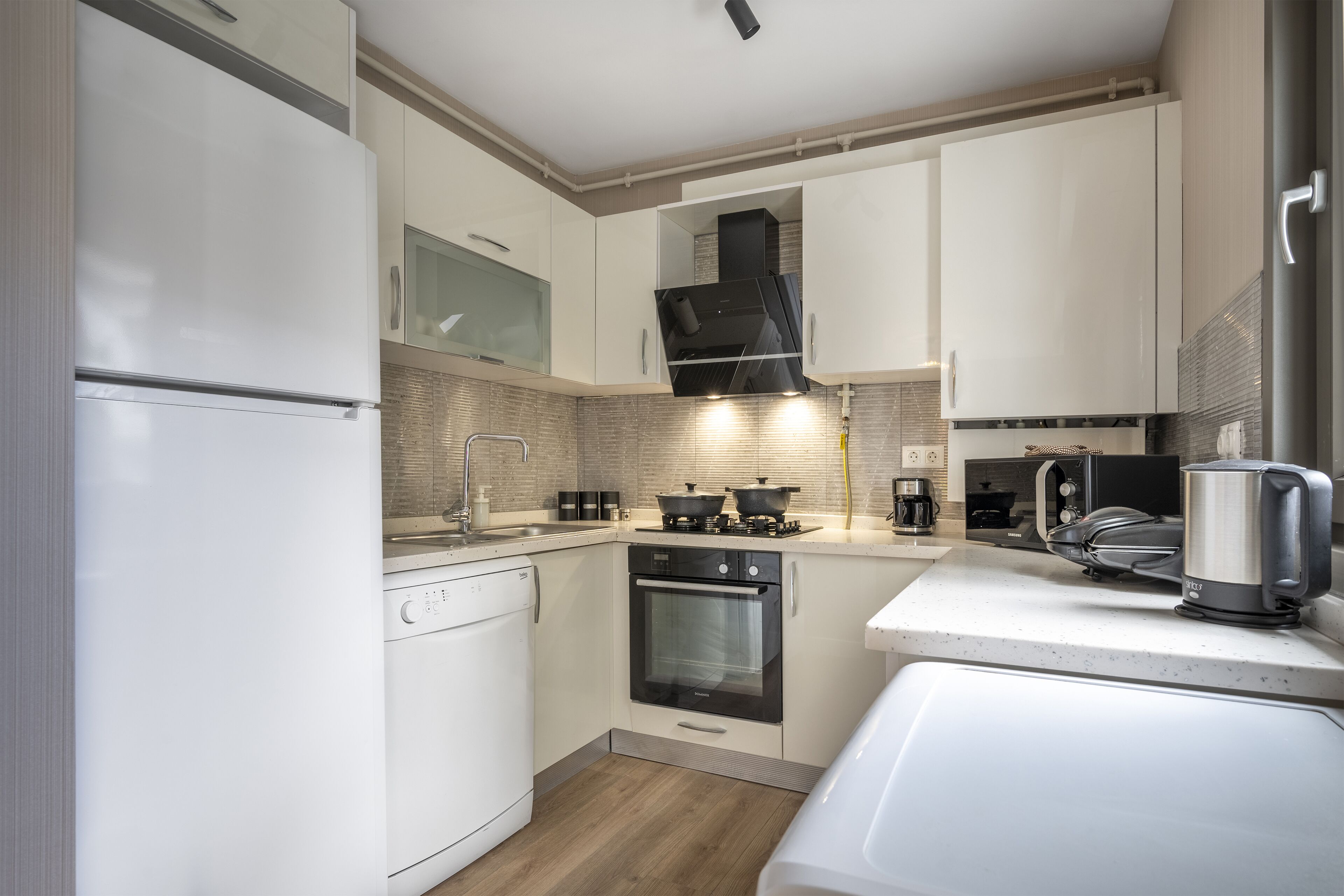 A modern kitchen with white cabinetry, a built-in oven, a microwave, and a kettle.