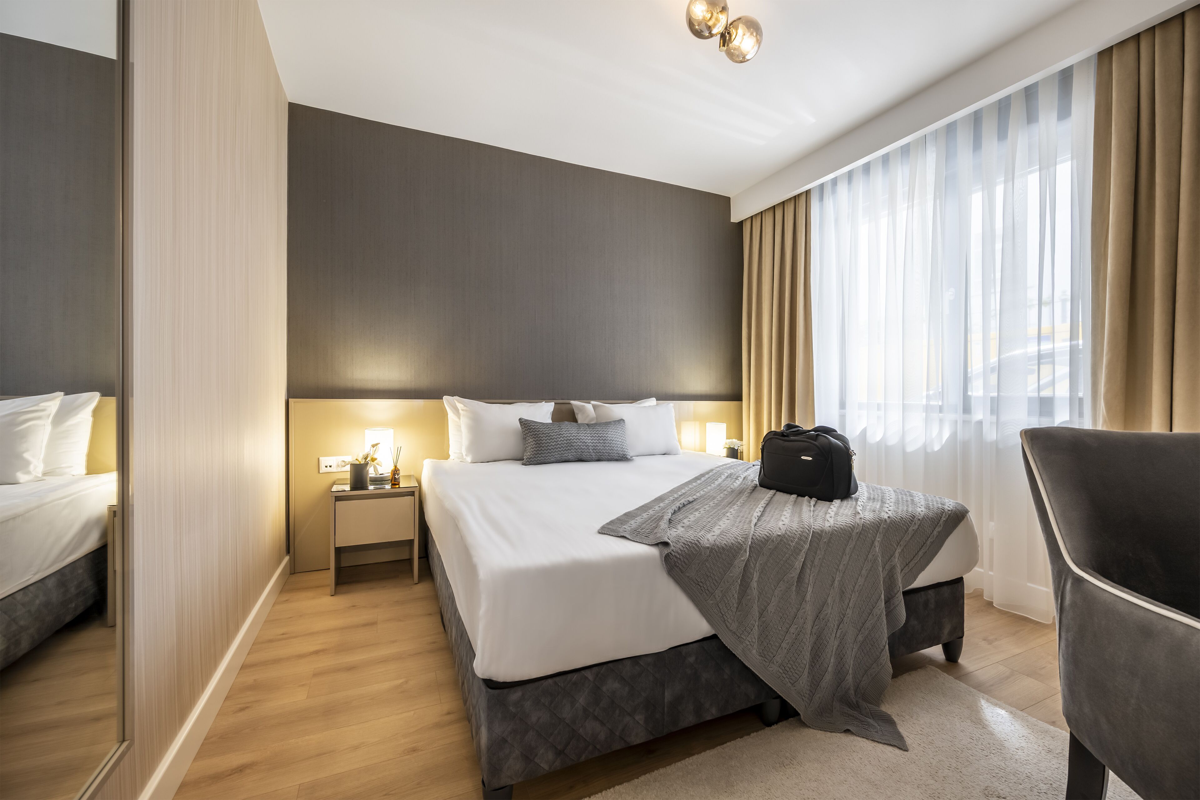 Una habitación de hotel con una cama grande, mesitas de noche, una silla y una ventana con cortinas.