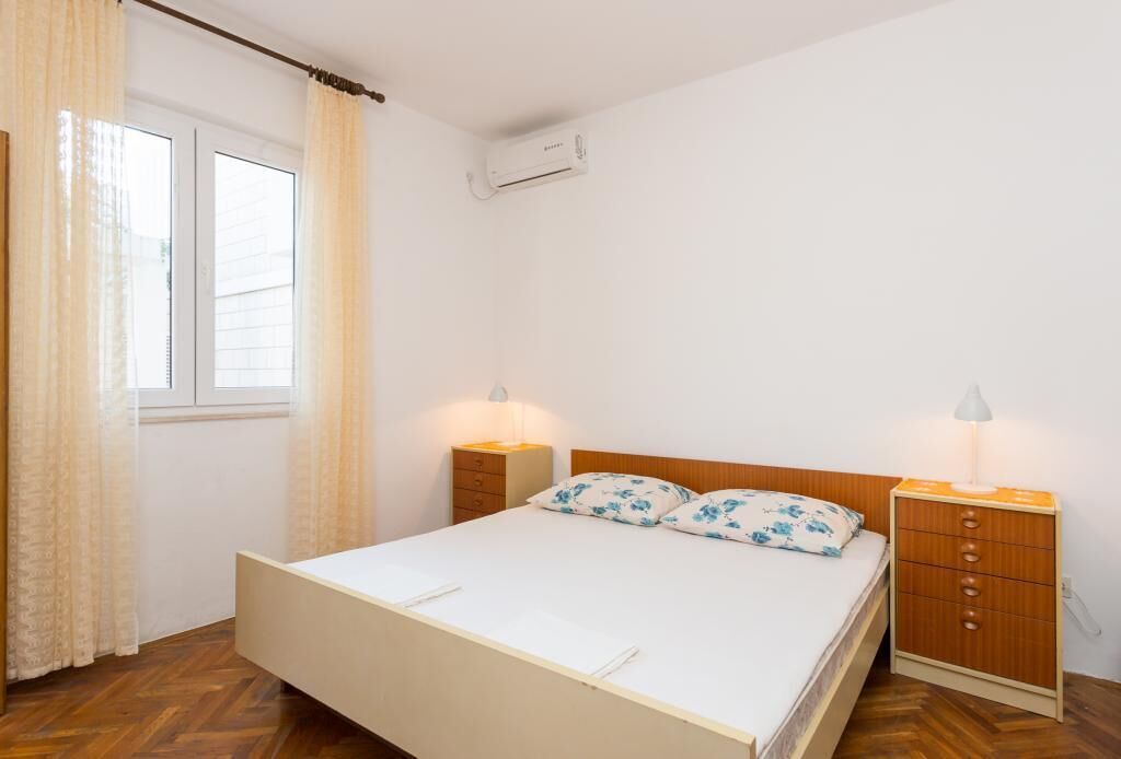 Une chambre avec un lit simple, deux tables de chevet, une commode, une fenêtre avec des rideaux et un appareil de climatisation.