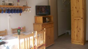 Ein kleiner, gemütlicher Raum mit einem Holzkabinett, einem Fernseher und einem Esstisch mit Stühlen.