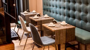 Un restaurant avec des banquettes recouvertes d’un tissu vert et plusieurs tables accompagnées de chaises.