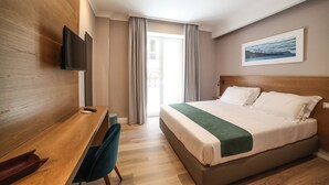 Une chambre d’hôtel avec un lit, un bureau, une chaise, une télévision et une fenêtre avec des rideaux.
