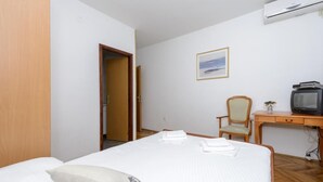 Hotellihuone, jossa on sänky, tuoli, kirjoituspöytä, jossa on televisio, ja taulu seinällä.