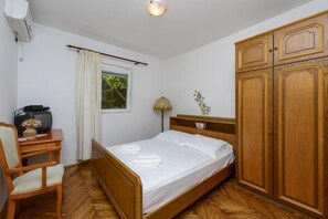Ein Schlafzimmer mit einem hölzernen Bett, einem Schreibtisch mit Radio, einem Kleiderschrank und einem Fenster mit Vorhängen.