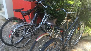 A bicycle parked next to a red planter, with a gravel ground and greenery in the background. - L'Ecrin de L'Ocean, 80 mètres de la mer (Le Pouliguen)