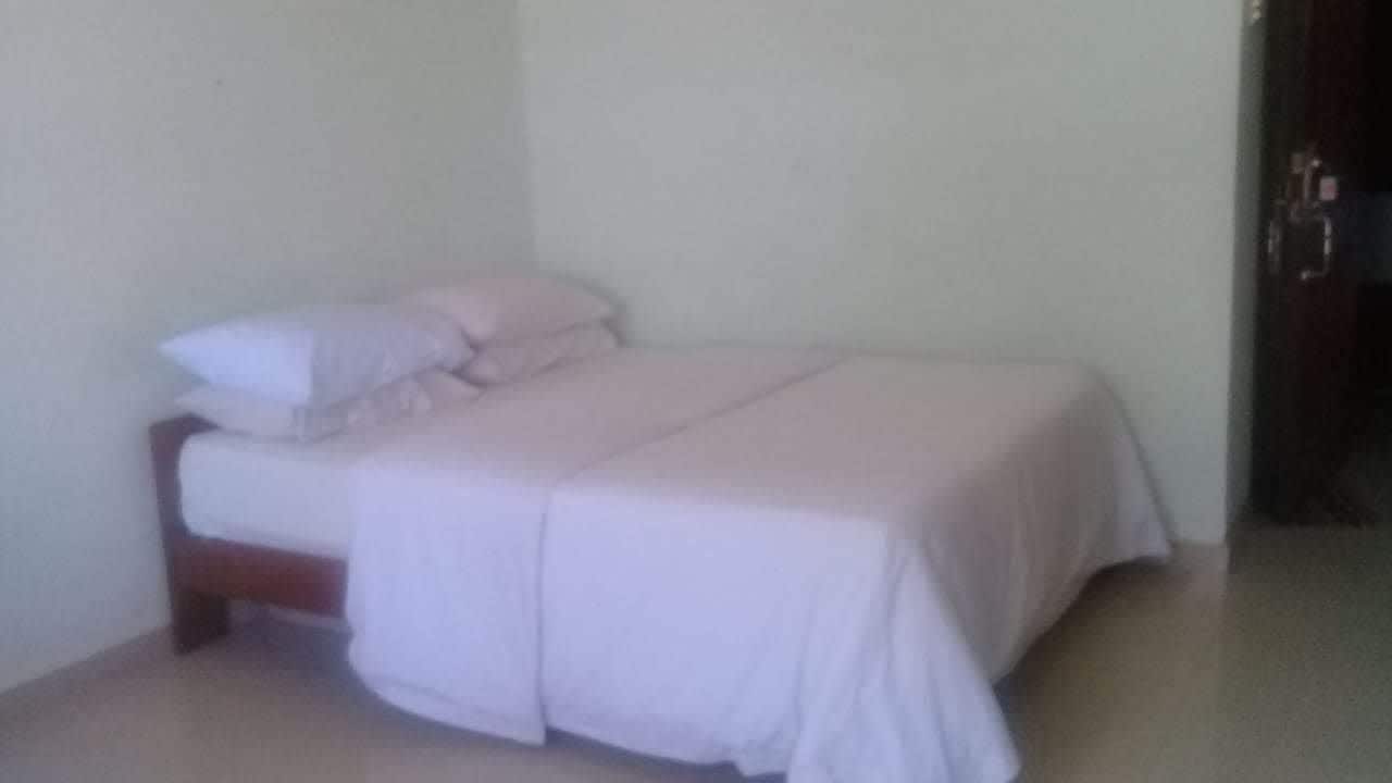 A small, single-bed room with a wooden headboard, white bedding, and a plain wall.