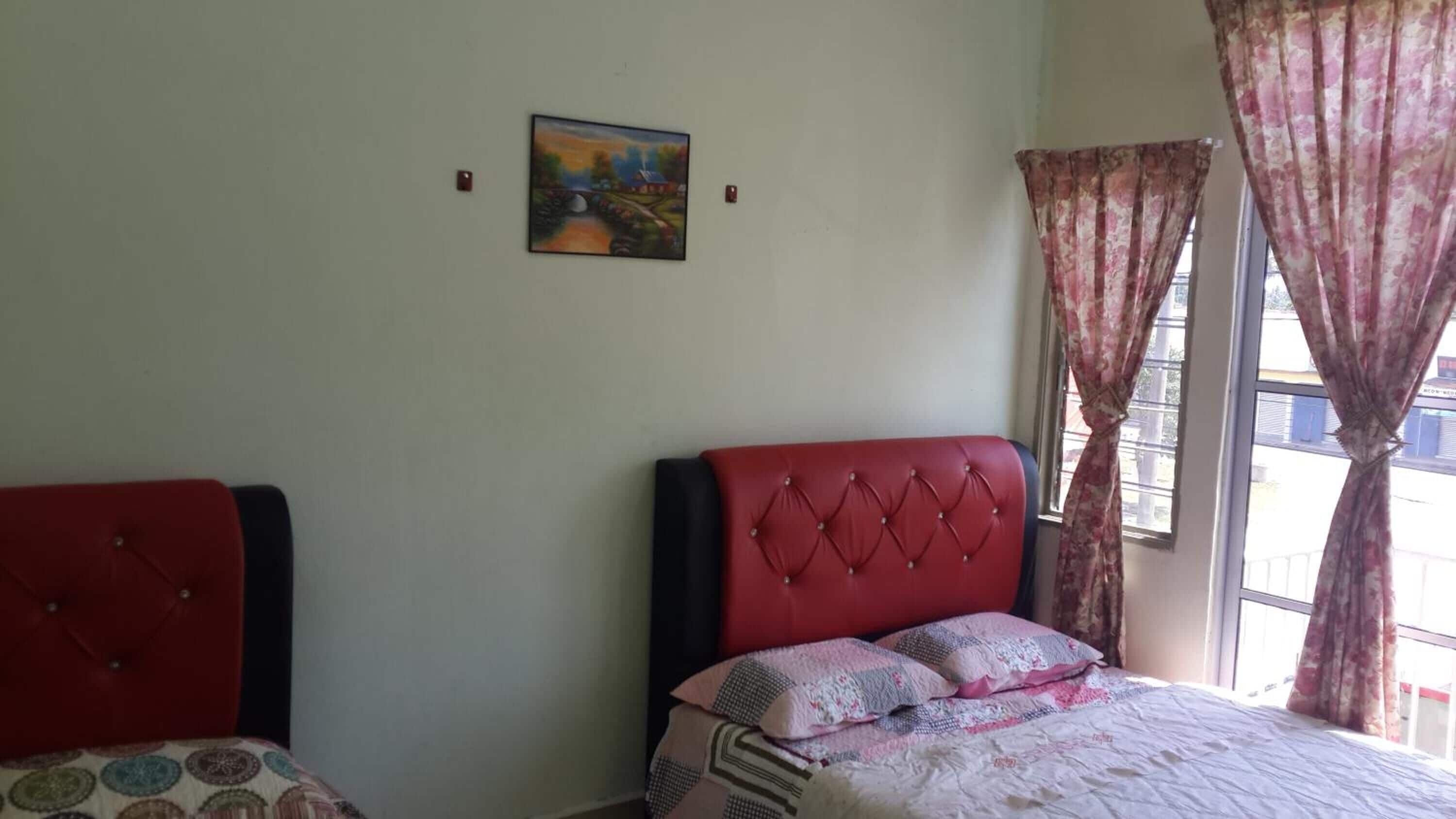 A bedroom with a bed, a red headboard, a window with curtains, and a painting on the wall.