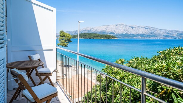 Un balcone con vista su un mare cristallino e una montagna innevata all'orizzonte.