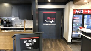 A modern pizza restaurant interior with a welcome sign, a Coca-Cola refrigerator, and a counter with a coffee machine. - Torrent River Inn (Hawke's Bay)