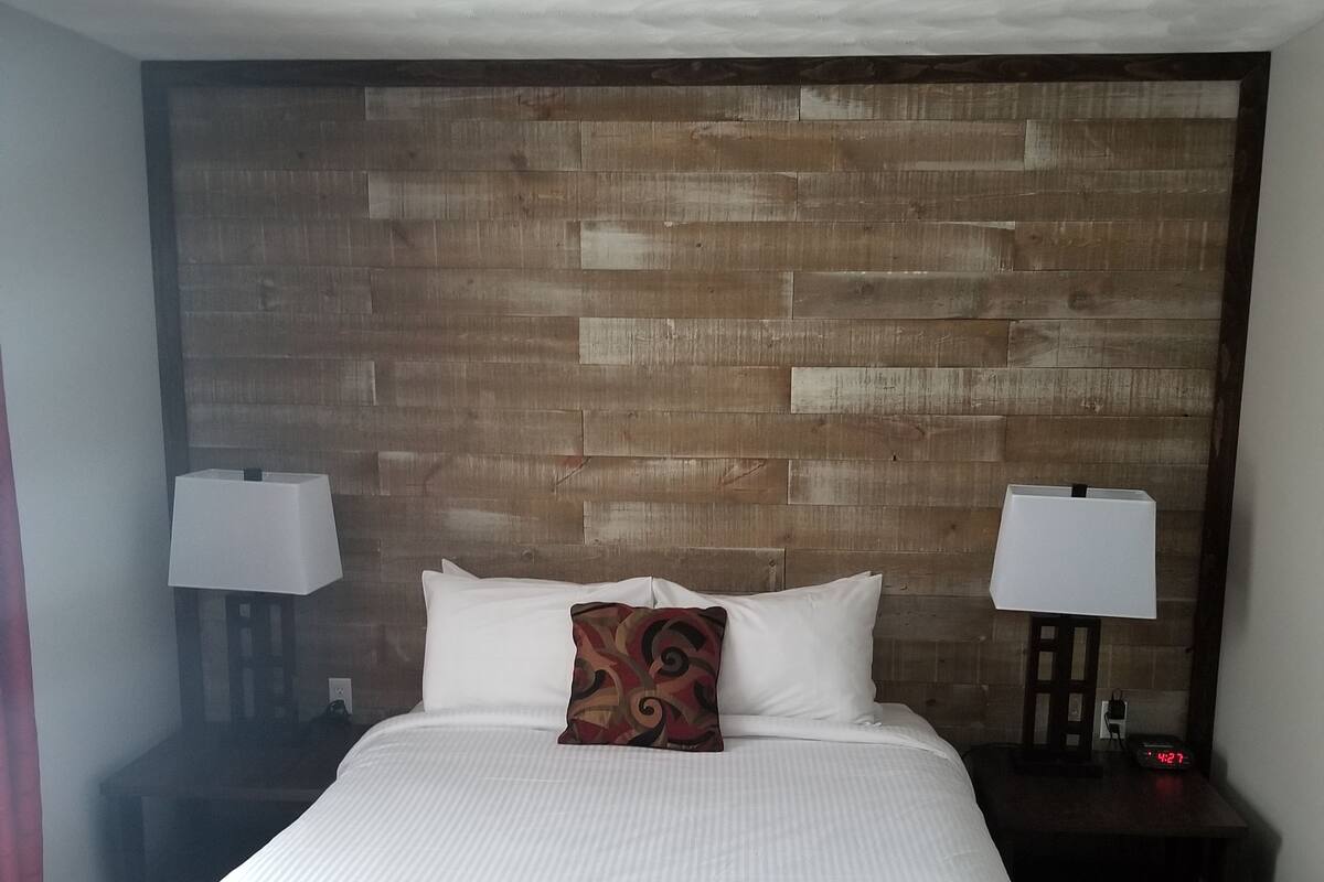 Una habitación de hotel con una cama grande, dos mesitas de noche con lámparas y un cabecero de madera.