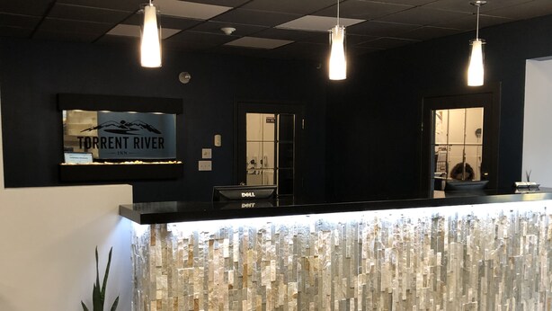 A reception desk with a stone-textured backdrop, overhead pendant lighting, and a sign reading "Torrent River Inn". - Torrent River Inn (Hawke's Bay)
