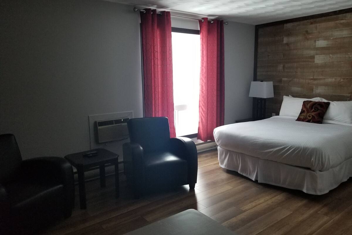 Una habitación de hotel con cama, una silla, una mesita y un ventanal con cortinas rojas.