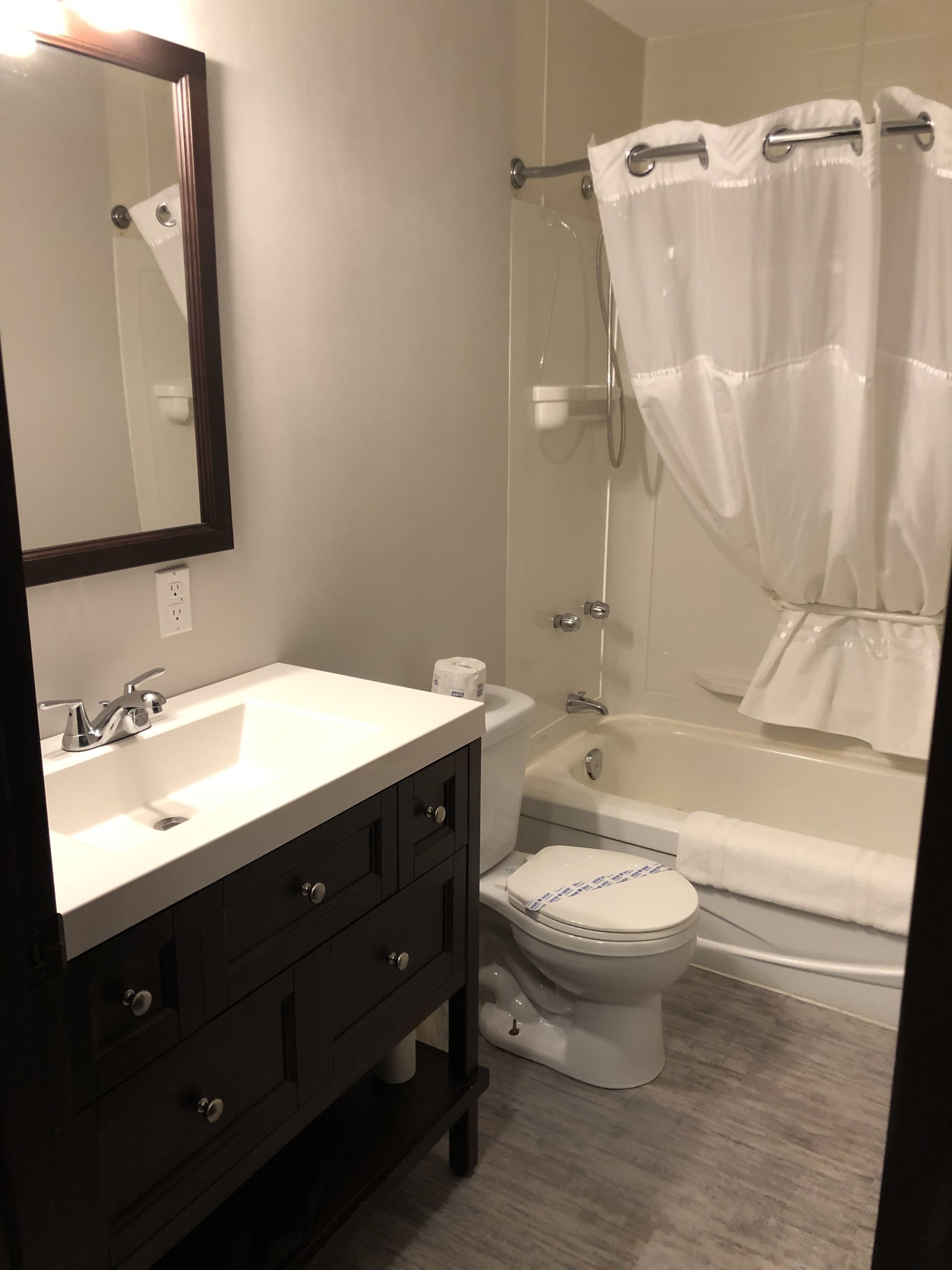 A modern bathroom with a white sink, dark vanity, toilet, and bathtub.