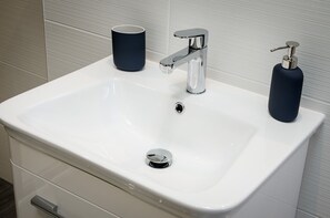 A white bathroom sink with a chrome faucet, a soap dispenser, and a cup. - Pen-y-Ghent (Carnforth)