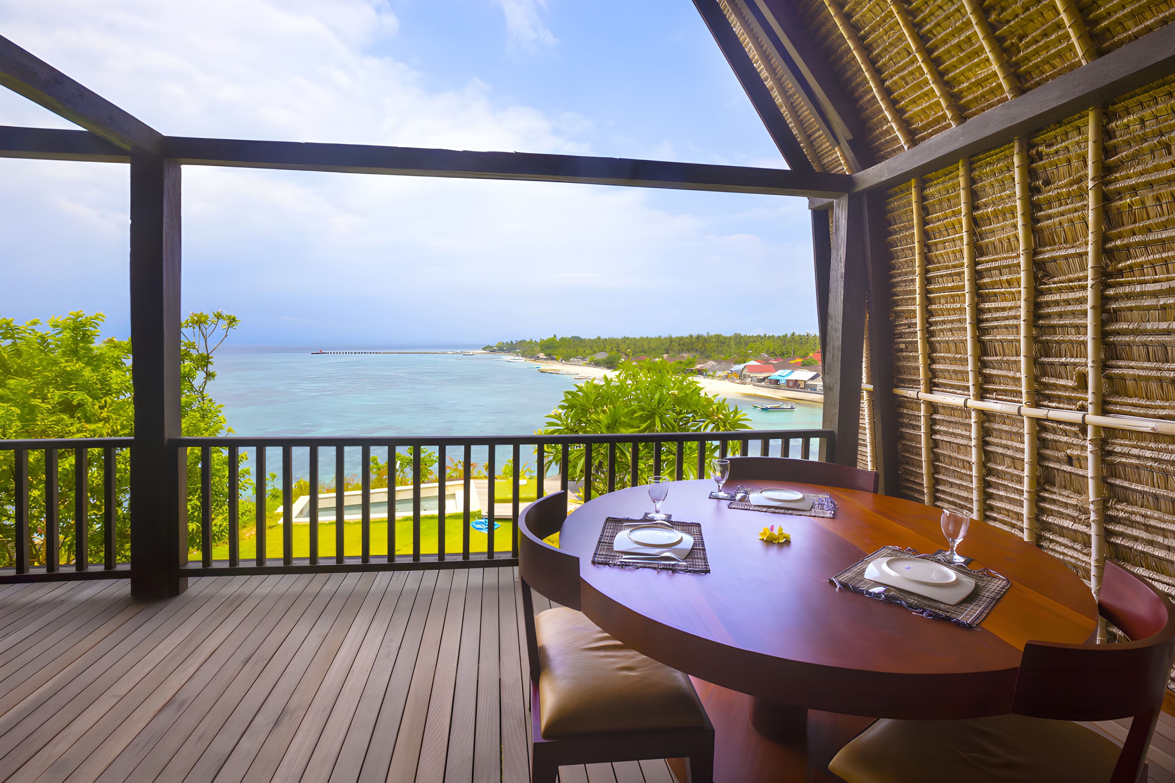 A wooden deck with a table set for dining, overlooking a beach and ocean.