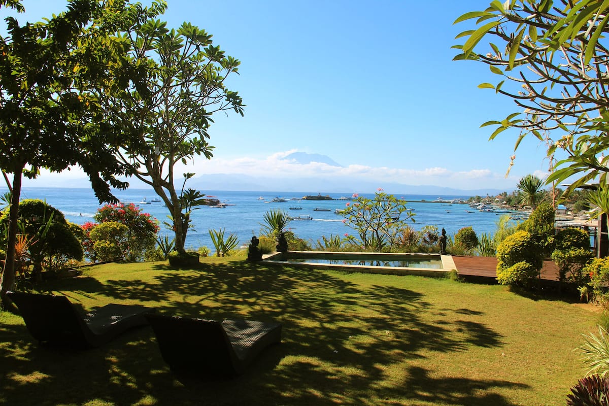 A garden with a pool, chairs, and a view of the sea and a mountain.