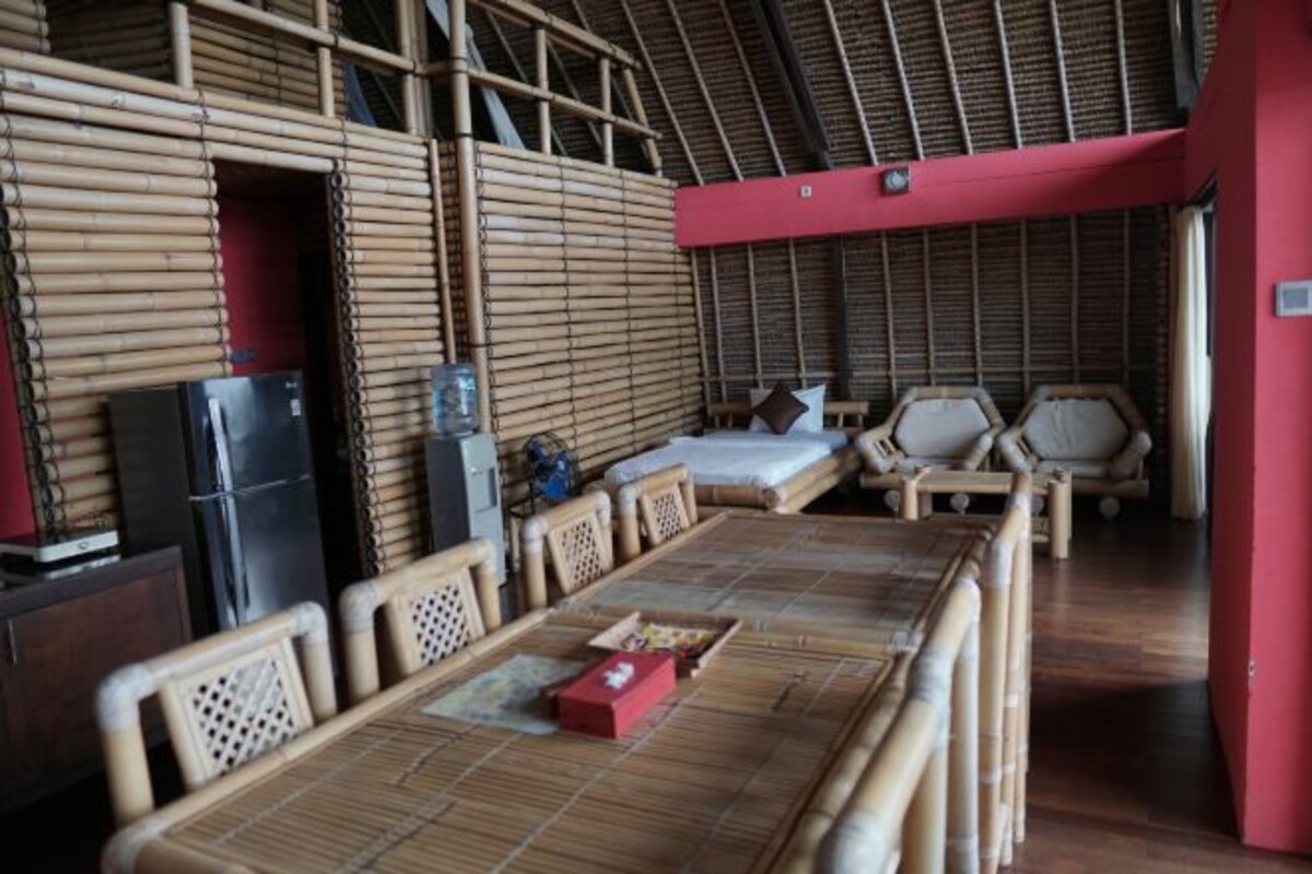 A room with a long table, chairs, a bed, and a small kitchen area.