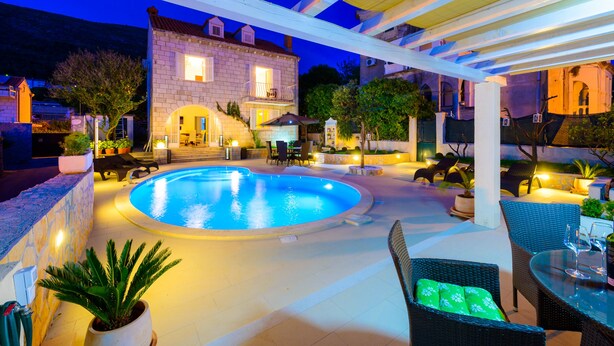 Ein Poolbereich mit einem Haus aus Stein im Hintergrund, Gartenmöbel und einer Pergola.