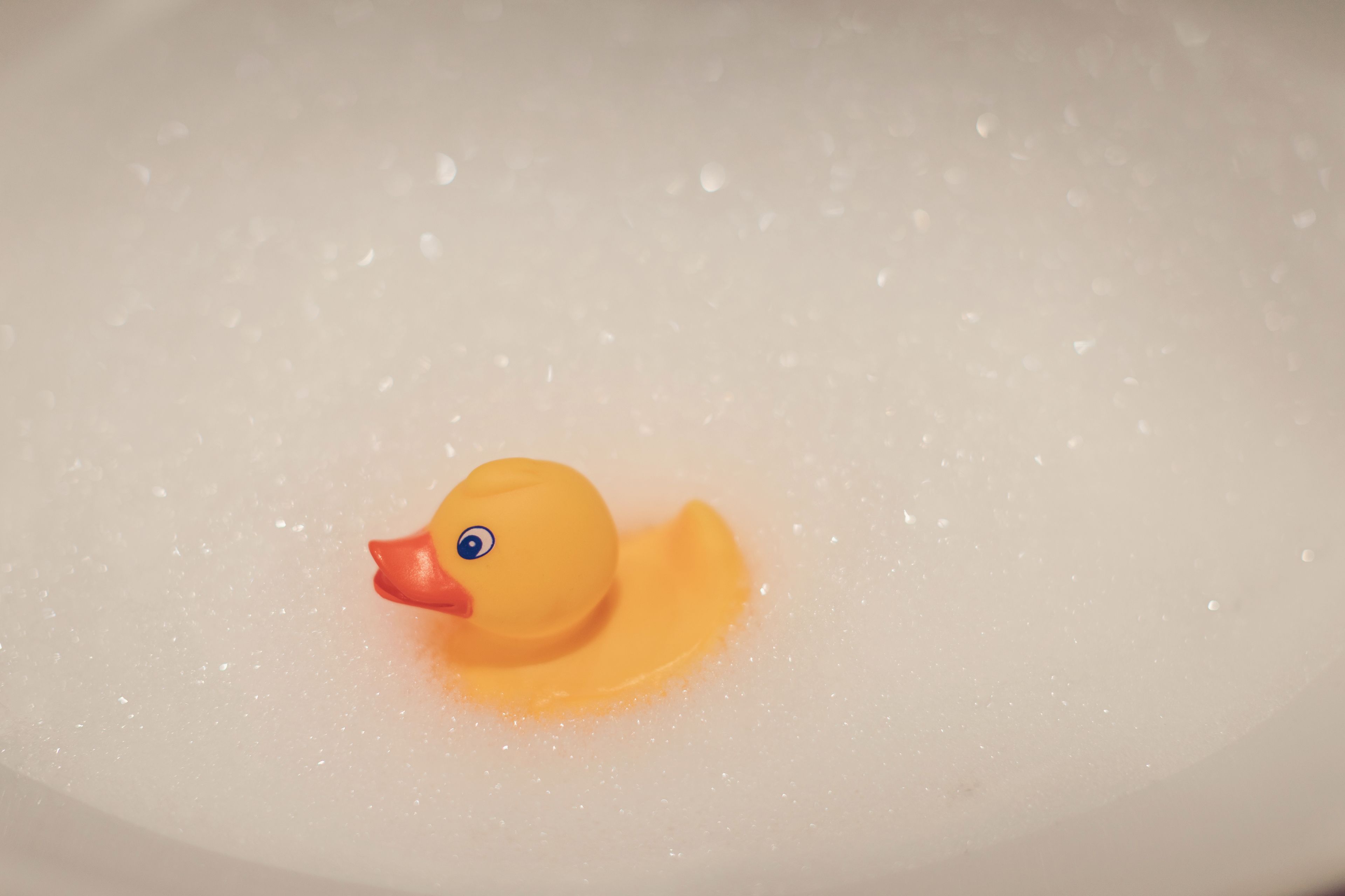 A yellow rubber duck floating in a bathtub filled with bubbles.