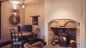 A cozy room with a stone fireplace, a round table with chairs, a leather sofa, and a decorative mirror. - The New Inn - Yealand (Carnforth)