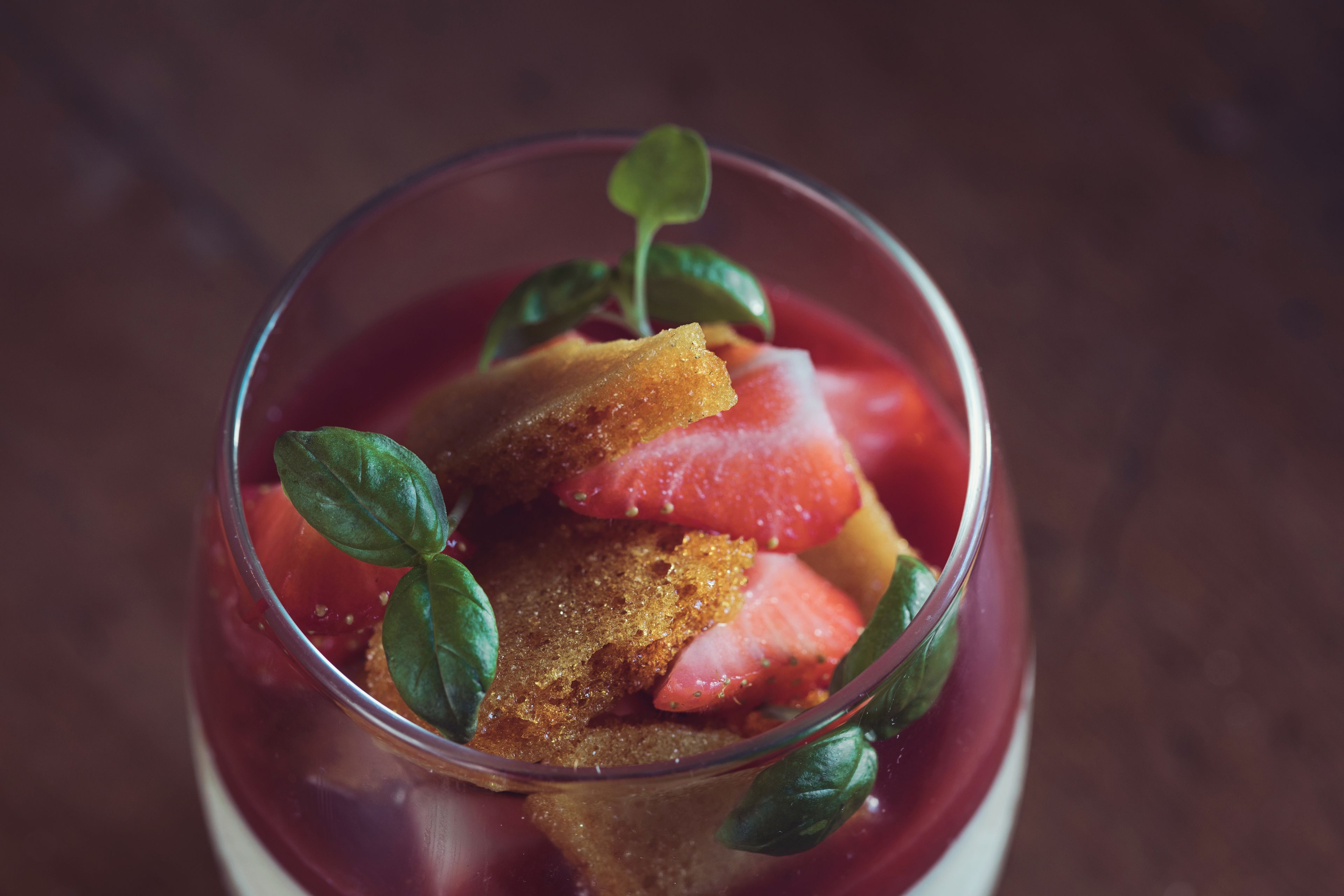 A dessert in a clear glass with strawberries and a piece of cake, garnished with a leaf.