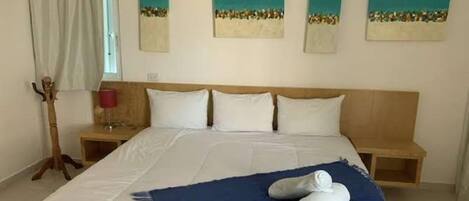 Habitación de hotel con una cama grande, dos mesitas de noche, un cabecero de madera y obras de arte en las paredes.