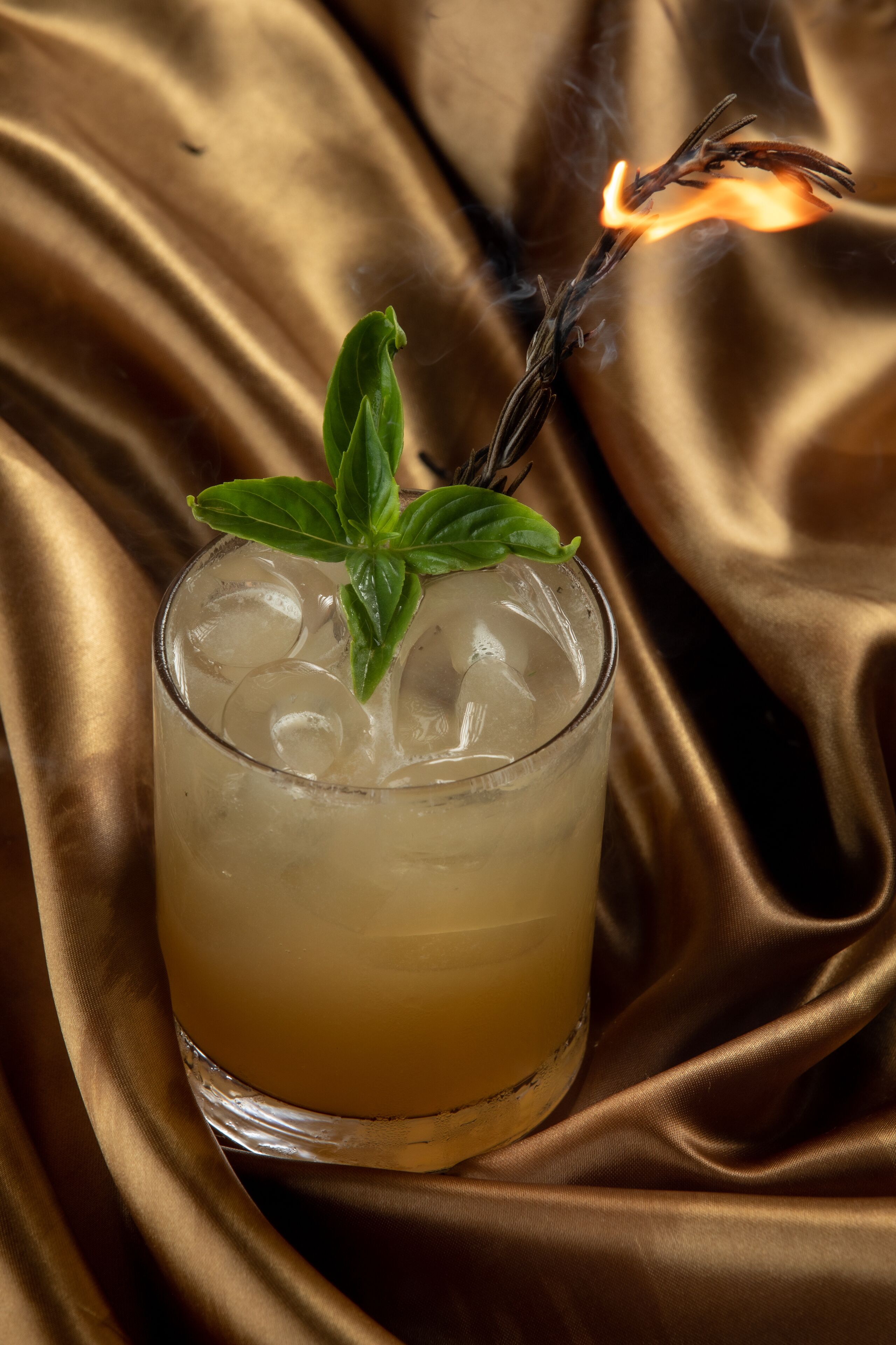 A glass with ice cubes and a sprig of mint on a golden fabric background.