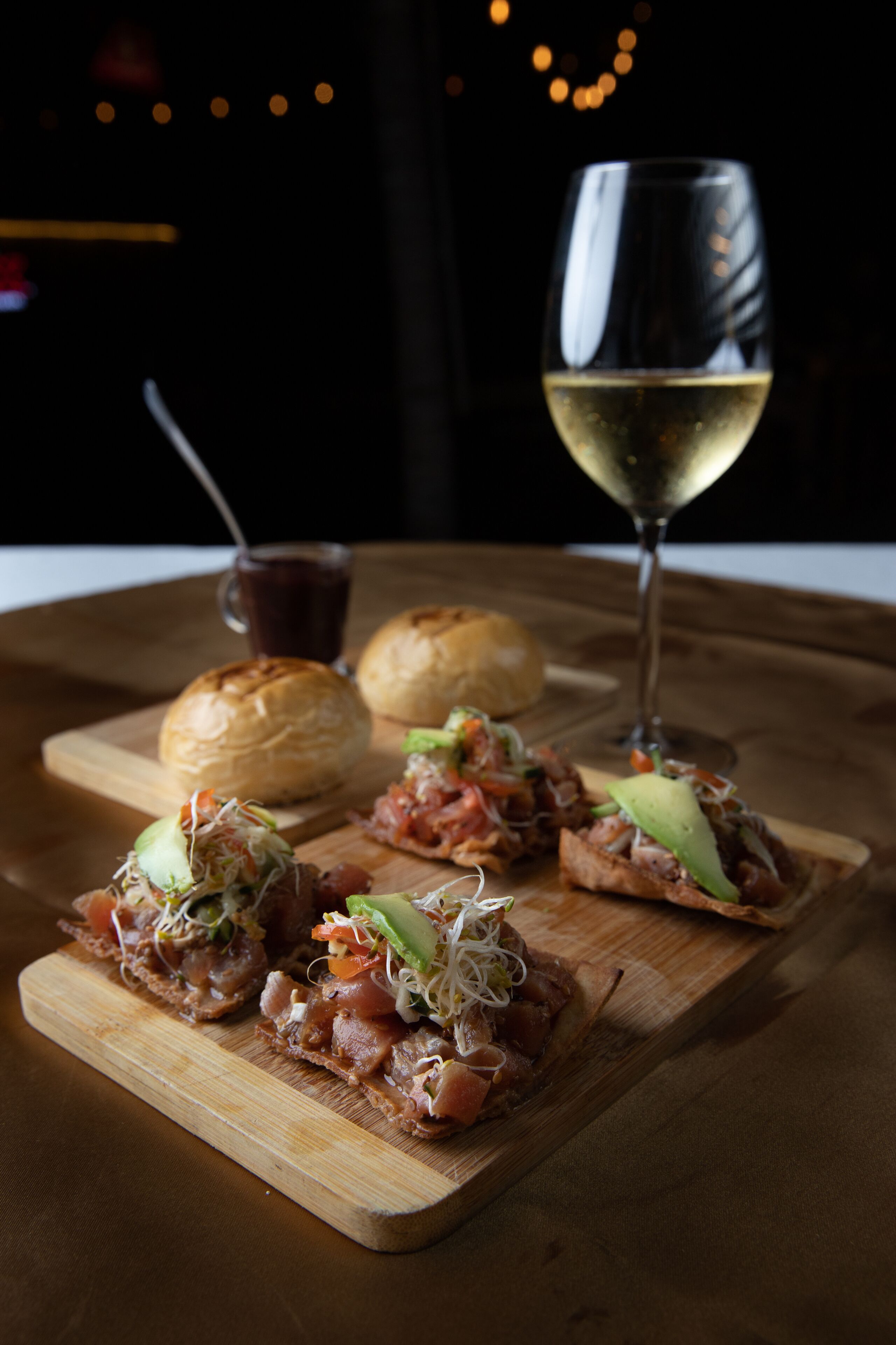A wooden board with food items and a glass of white wine on a table.