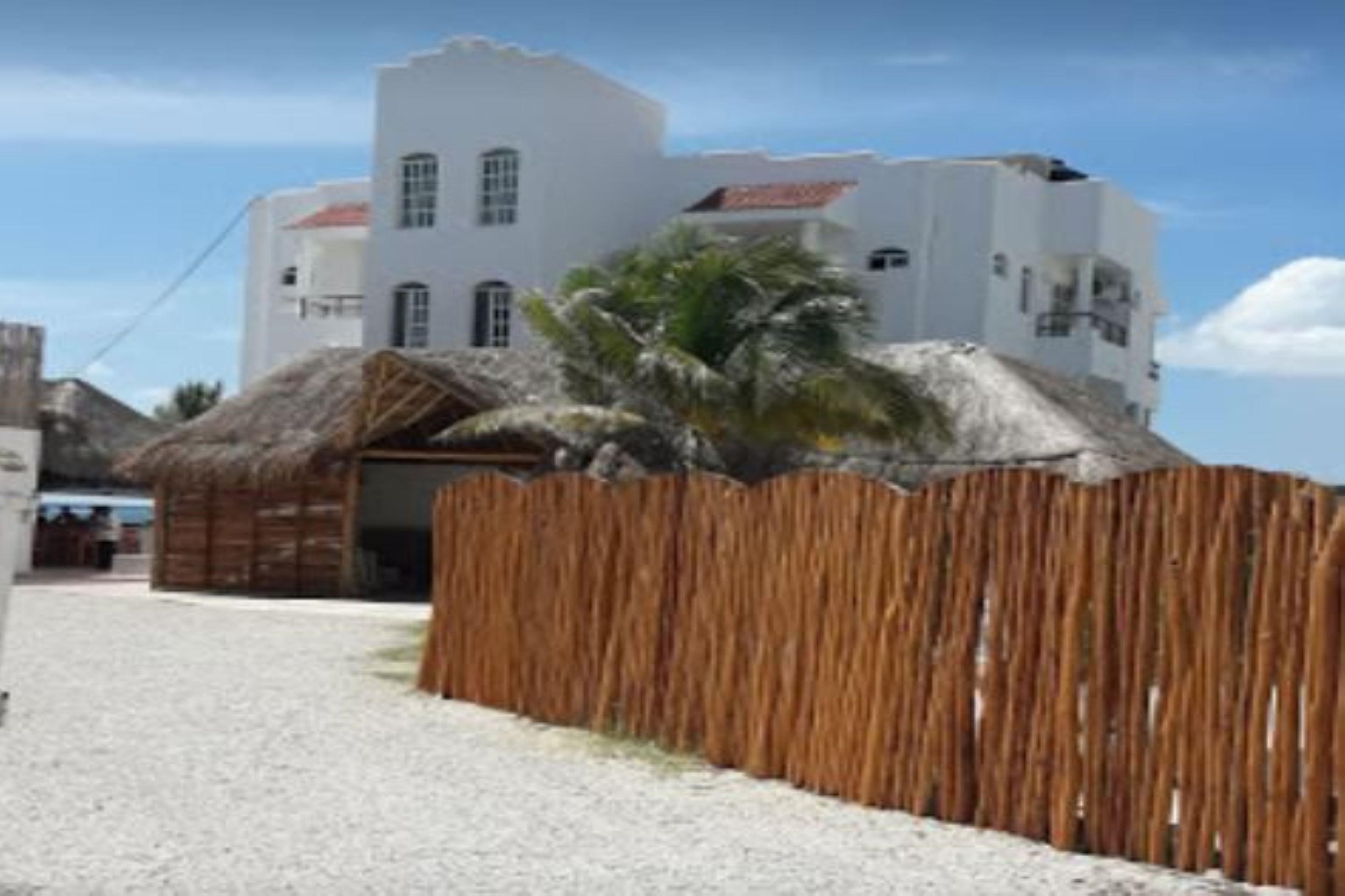 A white building with a red-tiled roof, a wooden fence, and a palm tree.