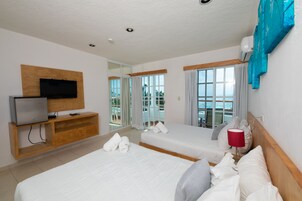 Habitación de hotel con dos camas, televisión, aparador de madera y balcón con vistas.