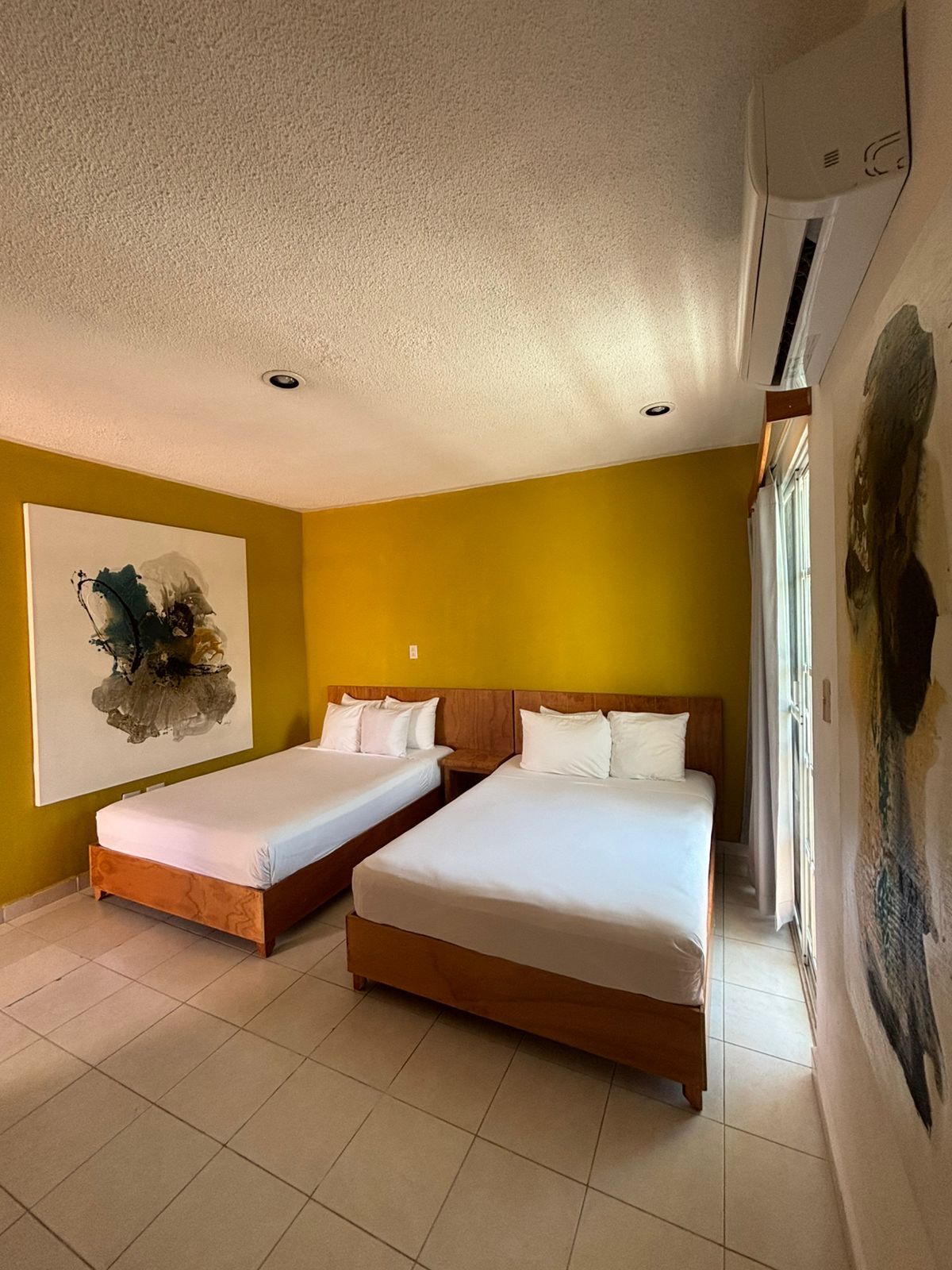 Habitación de hotel con dos camas, un ventilador de techo y un ventanal grande.