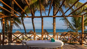 A wooden deck with a hammock and a towel, overlooking a beach with palm trees and thatched umbrellas. - Hotel & Beach Club Ojo de Agua (Puerto Morelos)