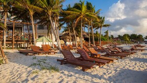 A beach with wooden lounge chairs and palm trees. - Hotel & Beach Club Ojo de Agua (Puerto Morelos)