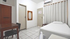 Een hotelkamer met een bed, een bureau, een stoel, een spiegel en een airconditioning.