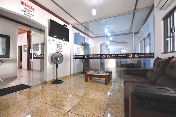 Um hall de hotel com balcão de recepção, um ventilador, uma mesinha de centro e um sofá.