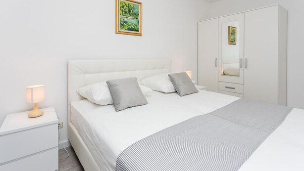 A bedroom with a bed, a nightstand, a wardrobe, and a painting on the wall. - Apartment Dupčić - Two Bedroom Apartment with Balcony (Dubrovnik)