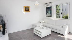 A modern living room with a white sofa, a glass coffee table, and two paintings on the wall. - Apartment Dupčić - Two Bedroom Apartment with Balcony (Dubrovnik)