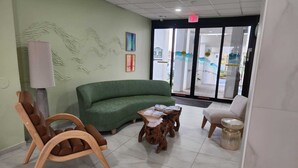 A reception area with a green sofa, wooden chairs, a small wooden table, and a lamp.