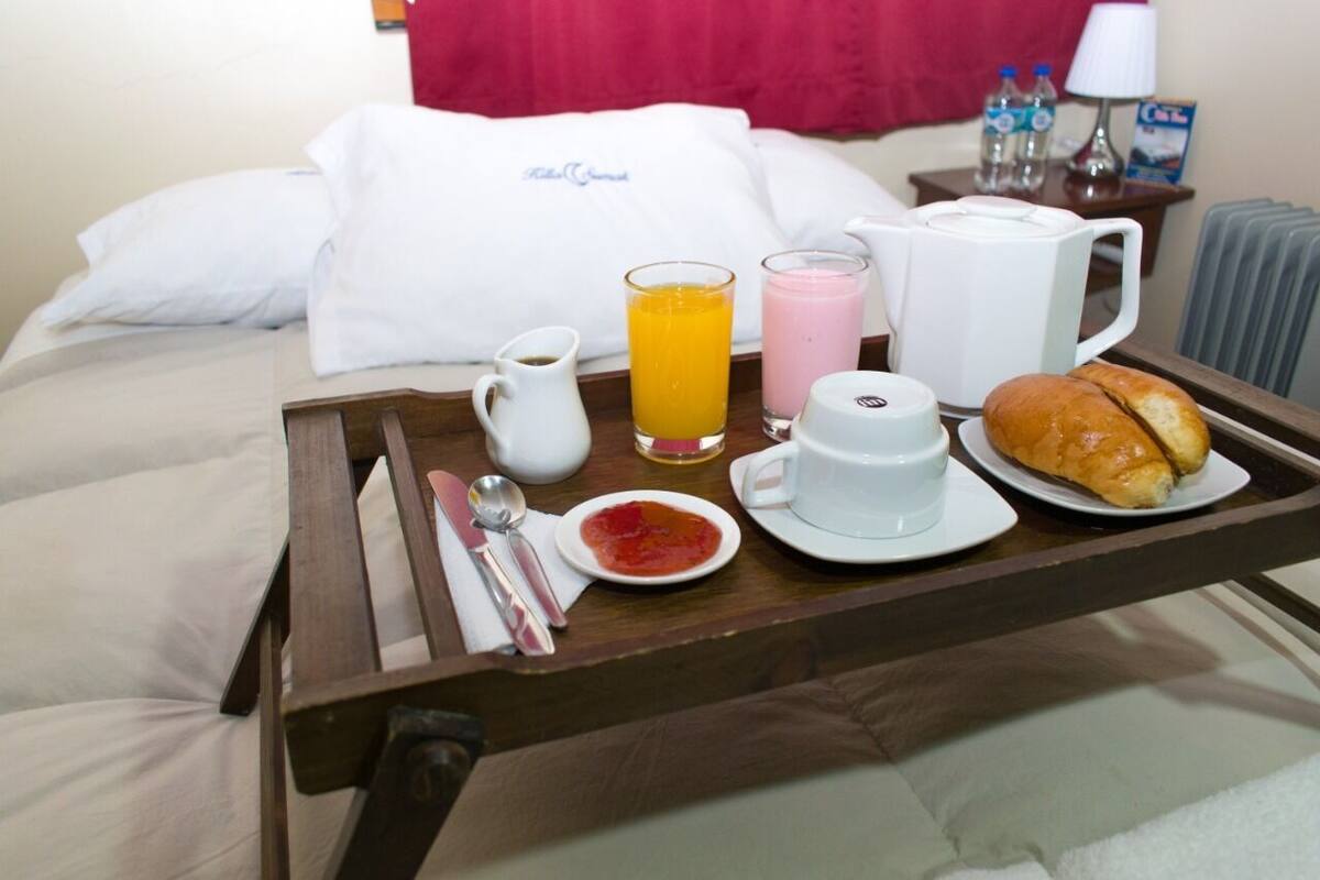 Un plateau de petit-déjeuner avec du jus, du café, un croissant et un pot de confiture, posé sur un lit.